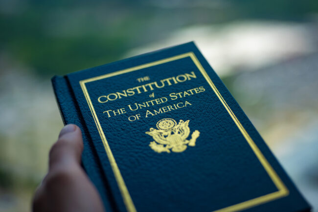 The Constitution of The United States of America book in hand on blurred background.