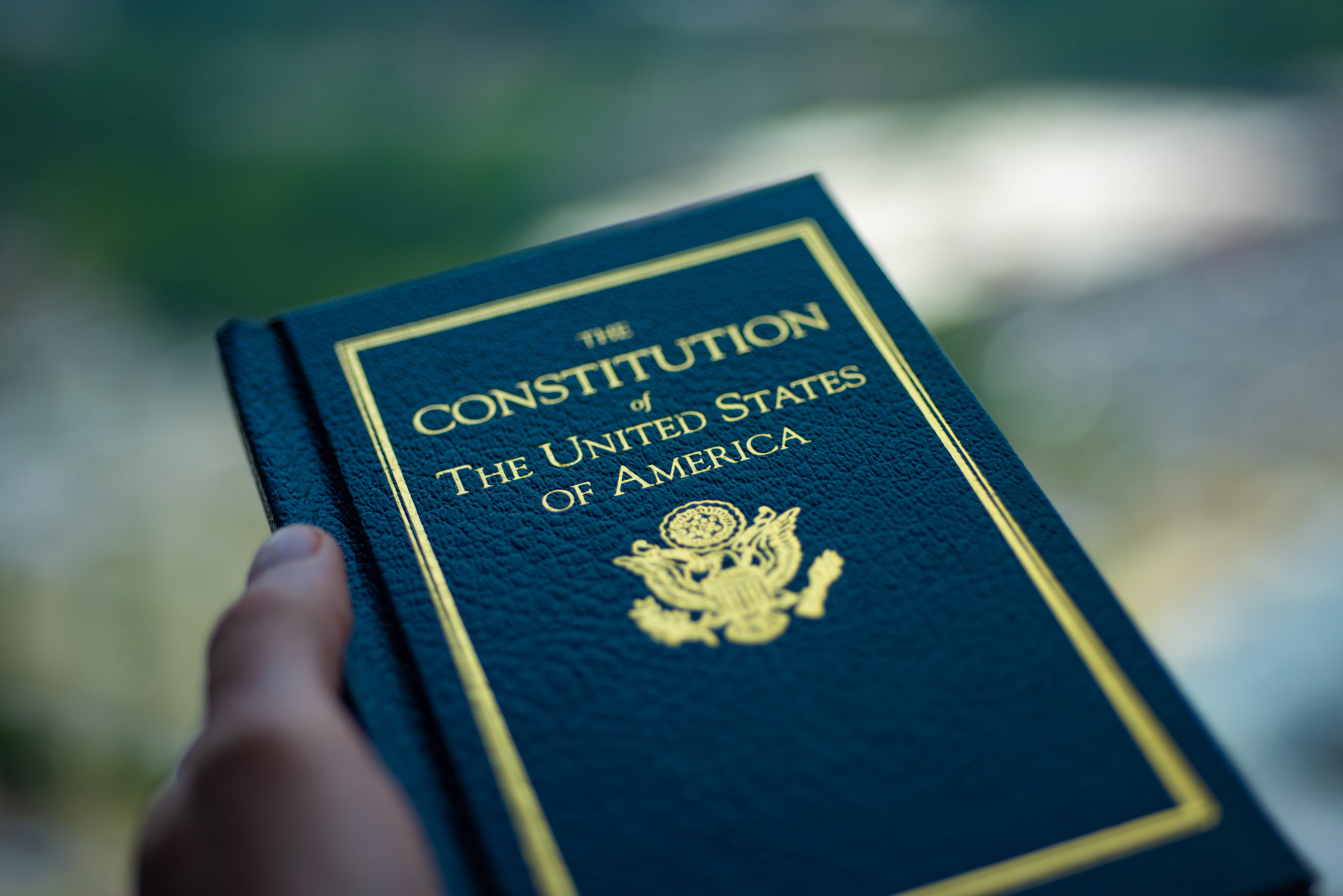 The Constitution of The United States of America book in hand on blurred background.